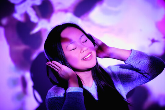 Stock photo of cool asian woman listening to music in her room with colorful lights.