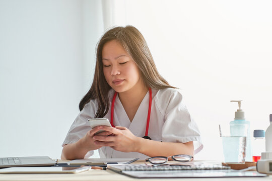 Stock photo of asian female doctor using her phone in her desk at home.