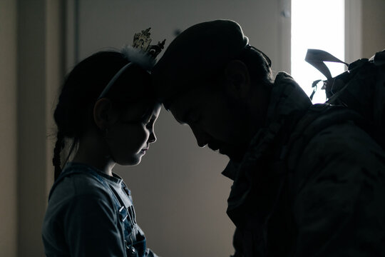 Side view silhouette of upset girl touching dad with forehead while seeing off dad to war
