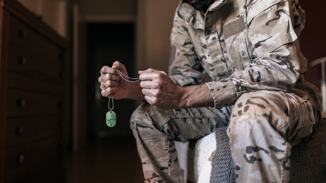 Low angle of a faceless soldier, holding the name badge, while preparing for military service at home.