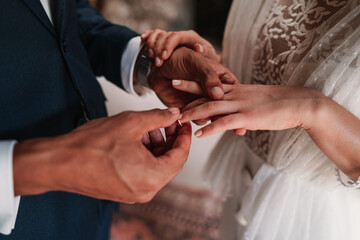 High angle side view of cropped unrecognizable ethnic groom putting ring on finger of bride in fancy wedding gowns holding hands gently with affection