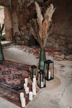 Aged building with fluffy dry plants in vases near burning candles and lanterns on ornamental carpet