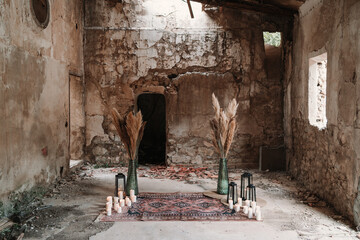 Aged building with fluffy dry plants in vases near burning candles and lanterns on ornamental carpet