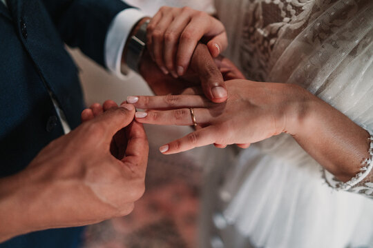 High angle side view of cropped unrecognizable ethnic groom putting ring on finger of bride in fancy wedding gowns holding hands gently with affection