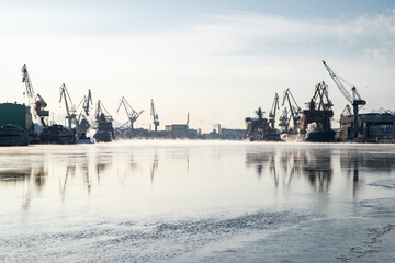 Cranes of of the Baltic shipyard on a frosty winter day, steam over the Neva river, smooth surface...