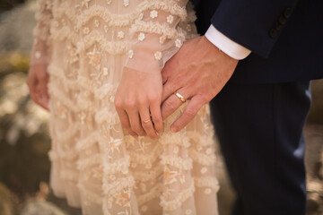 Newlywed Bride and Groom Gently Holding Hands Displaying their Engagement Ring and Wedding Rings Outside Her Dress has Ruffles and Sequins Professional Wedding Photography