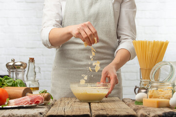 Cooking food, chef prepares creamy sauce with parmesan cheese, grated, frozen in motion on the background of the kitchen with ingredients. Delicious food, menu for cafe or restaurant