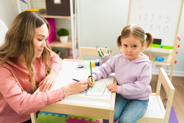 Portrait of a preschool girl coloring together with a female teacher