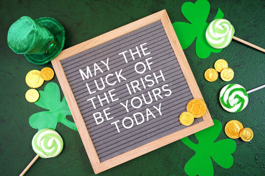 Happy St Patrick's Day felt letterboard message board styled with leprechaun hat, shamrocks, and chocolate gold coins, on a textured green background. May the Luck of the Irish greeting.