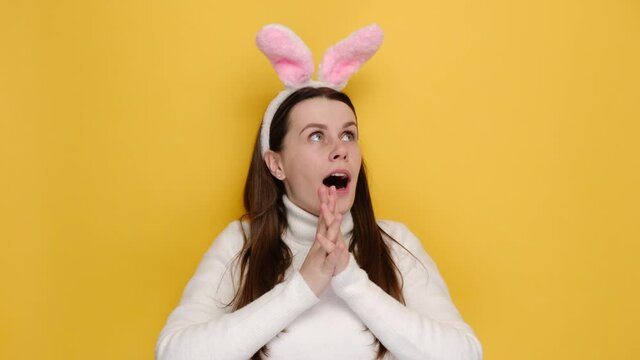 Surprised shocked young female 20s in pink bunny fluffy ears say wow put hands on cheeks head, wears white jumper, isolated on yellow studio background. Easter holiday and people emotion concept