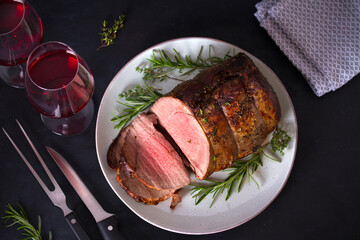 Sliced roast beef with herbs and red wine on dark background. Overhead horizontal photo