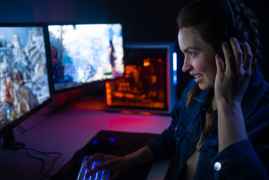 A Girl With Headphones Plays A Video Game On A Computer On Large Monitors. Gamer With Mouse And Keyboard. Online Games With Friends,win.Fun Entertainment.Teenagers Play Adventure Games.Neon Lighting