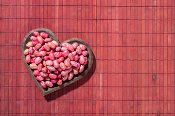 Fototapeta na wymiar Red kidney beans in heart bowl on red wood