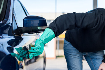 Lavado de coches. Detalle de la mano de un hombre con un guante verde limpiando su coche con una esponja.