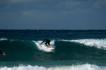 Obraz premium Male surfer catching a wave and doing a turn wearing a black wetsuit in winter time