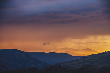 Atmospheric landscape with silhouettes of mountains with trees on background of vivid orange blue violet dawn sky. Colorful nature scenery with sunset or sunrise of illuminating color. Sundown paysage