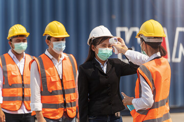 Factory woman worker in a face medical mask and safety dress used measures temperature at worker...