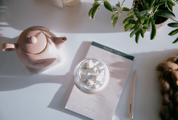 Flatlay Of Pink Teapot, Paper, Pen And A Glass Of Marshmallows
Viewed from above are a pink teapot, a glass filled with marshmallows that is on top of a pad a paper with a pink pen next to it a