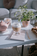 Fototapeta na wymiar Living Room With Coffee Table With Hot Chocolate Photo A white coffee table with a teapot, a lit candle, a house plant in a pink pot and a round glass with hot chocolate topped with marshmallows 
