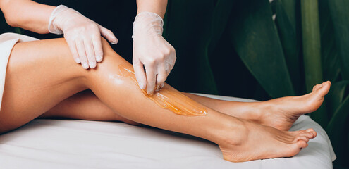 Leg waxing procedure at the spa salon with a caucasian woman lying on bed - obrazy, fototapety, plakaty