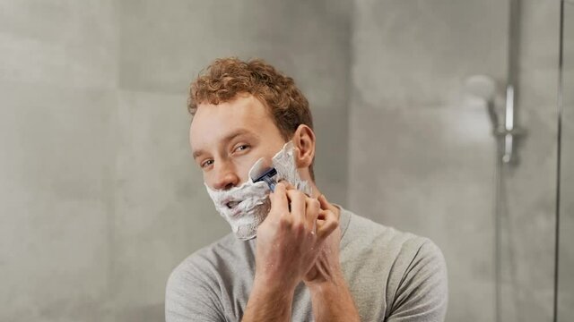 Handsome young guy shaves his beard with a razor