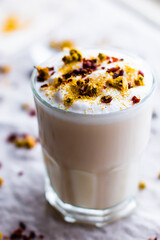 Pink tea latte in glass topped with foamy milk, rose hips, & chamomile