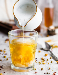 Foamy milk pouring into a glass filled with yellow chamomile tea