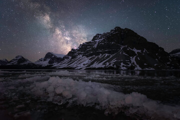 Ice blocks washed ashore Bow Lake with the Milky Way shining over the Canadian Rockies in the early Summer.
