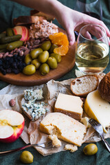 A hand reaching for white wine in a cheese board spread