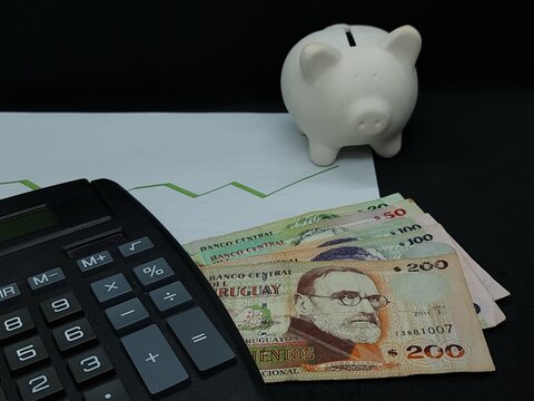 uruguayan banknotes, piggy bank and calculator on background with rising trend green line - Powered by Adobe