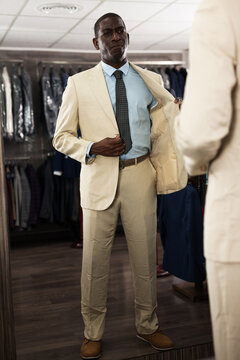 Confident male customer choosing fashion beige suit in mens store. High quality photo