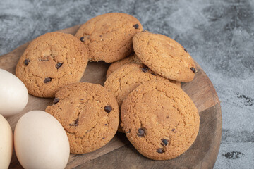 Oatmeal cookies with chocolate drops on a wooden board with eggs around
