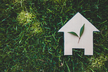 Naklejka premium green home and eco-friendly construction, house icon on green grass lawn under the sun with two leaves on top