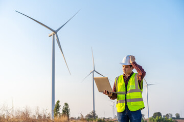 stressed male engineer having problem to working with laptop computer against wind turbine farm