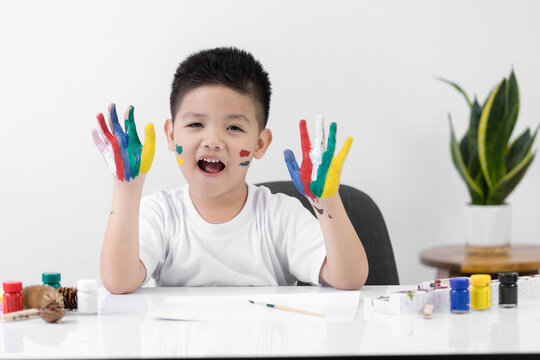 Smart little Asian boy having an idea while with painted hands at home. Learning and education of kid