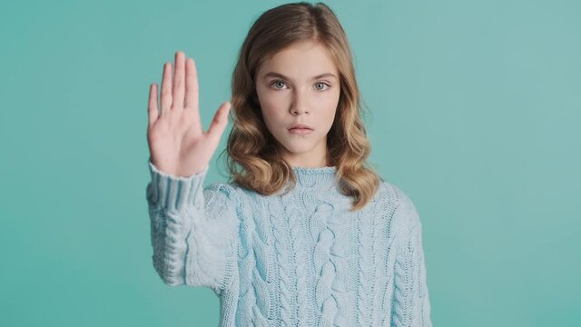 Serious blond teenage girl looking confident showing stop gesture rejects something on camera over colorful background. No gesture