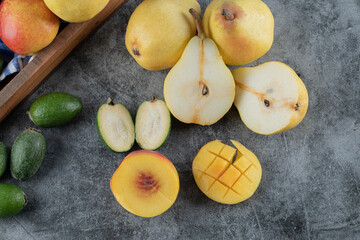 Green feijoa, peach and pears in a wooden tray and on the grey marble