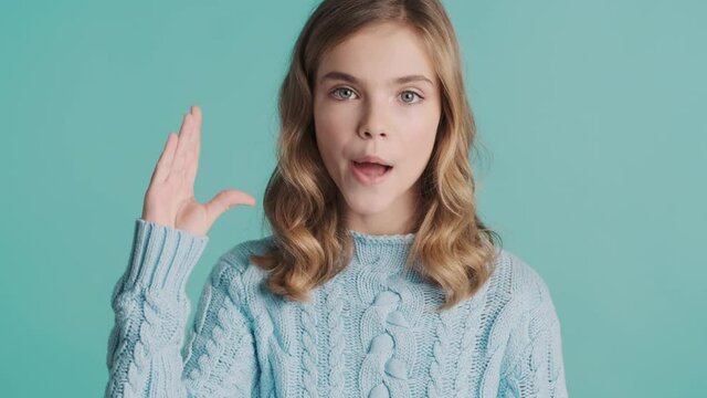 Bored blond teenager girl looking serious showing bla bla gesture on camera over colorful background