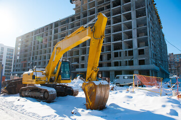 yellow excavator frozen on a construction site in the cold winter against the background of a new house