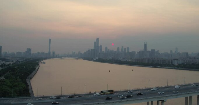 Silhouette of Guangzhou downtown district in far distance on sunset, with bridge over pearl river with heavy traffic. Slow aerial rise up.