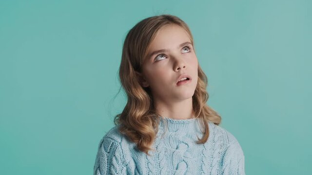 Annoyed blond teenage girl looking bored posing over blue background. Not interested expression