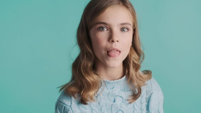 Pretty blond teenage girl with wavy hair showing tongue on camera and smiling over colorful background. Funny  girl