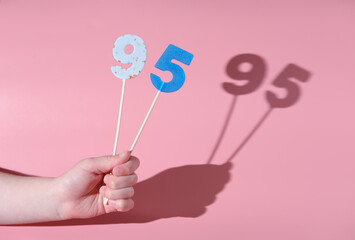 girl's hand holding a number 95 shaped lolipop. anniversary or birthday selebration. party sweet treats. pink background and direct light.