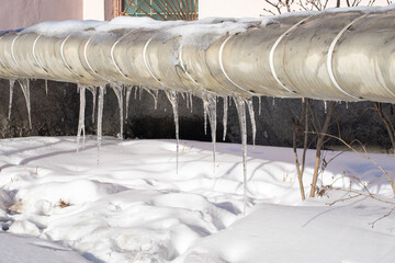 Very beautiful transparent icicles hanging from a snow-covered pipe. Spring melting snow. Icicles falling danger concept