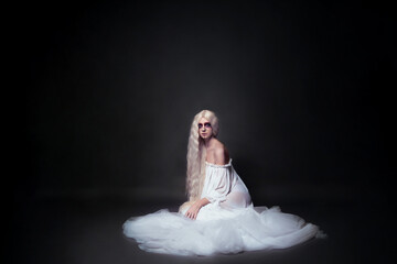 Fototapeta premium a concept photo of a beautiful young woman with bright makeup who plays the role of a priestess, spirit or ghost for Halloween. She is sitting in a white veil on a black background
