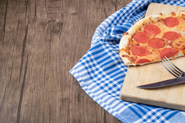 Pepperoni pizza slices on a wooden board with knife and fork around