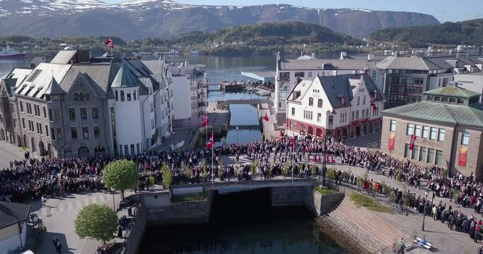 Descending, reveling aerial drone footage of marching people amongst art nouveau buildings, Brosundet bridge of Alesund, Norway's most beautiful town, during national, constitution day, 17th of May.