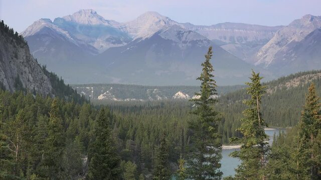 Expansive shot of Banff National Park. Snow capped mountains, lush green forest, and a crystal clear lake. Static shot.