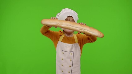 Little charming child girl dressed in apron and hat like chef cook baker breaking and eating fresh baguette on chroma key background. Concept of nutrition, family cooking school, children education