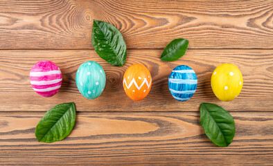 Group of cute colorful eggs decorated with paints on a wooden table and spring leaves. Concept of Easter and spring